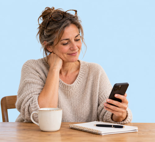 Femme souriante regardant son smartphone avec un café et un cahier